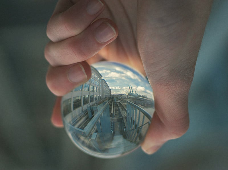 Zdjęcie zrobione przez szklaną kulkę trzymaną w dłoni w której odbija się widok na fabrykę