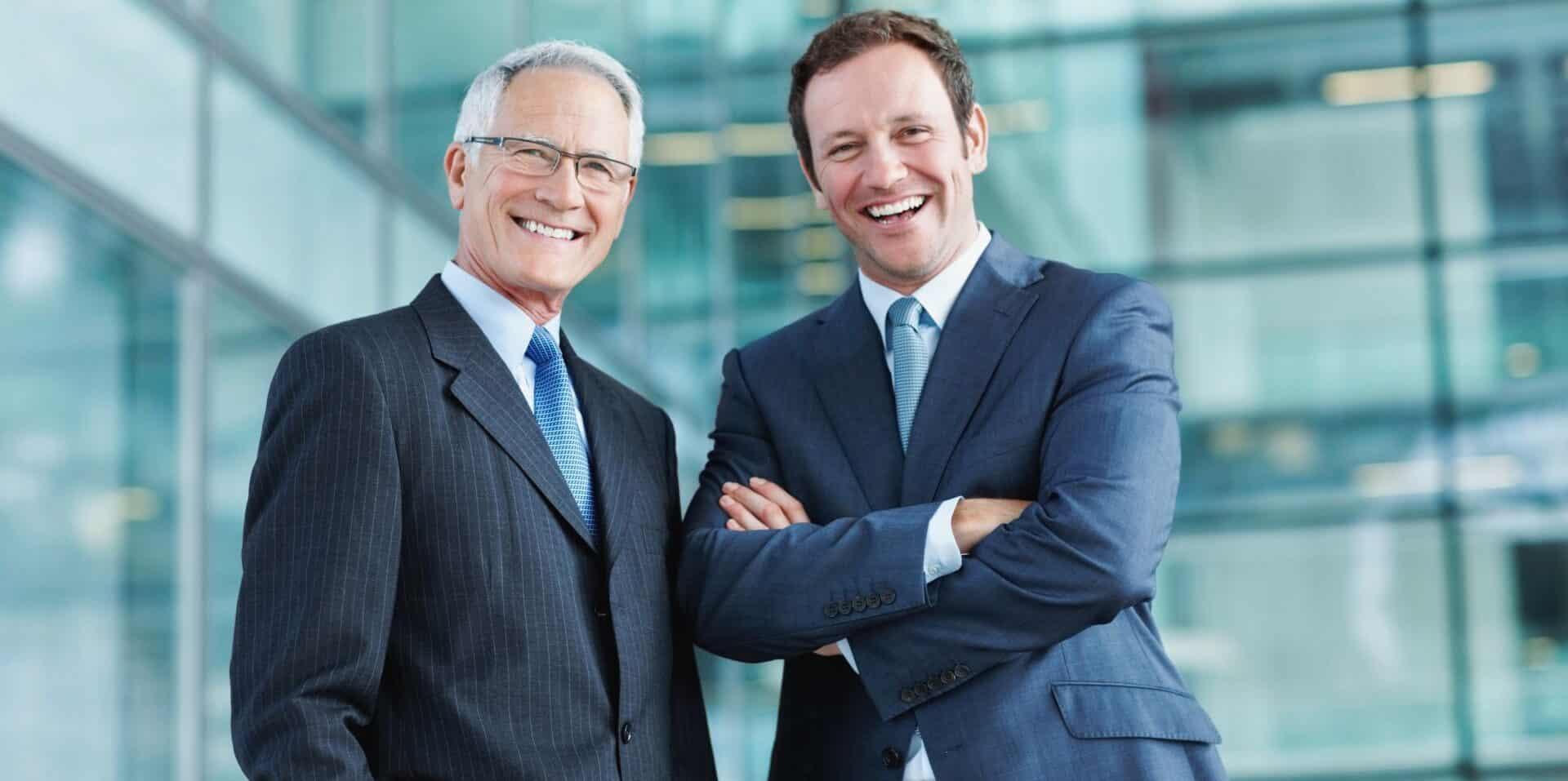 Dwaj mężczyźni w garniturach jeden starszy od drugiego obaj uśmiechnięci