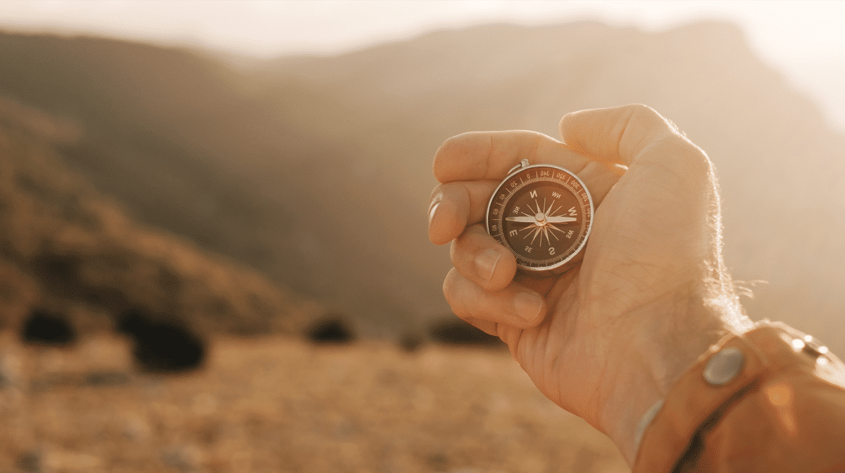 Dłoń trzymająca kompas z widokiem na góry w oddali