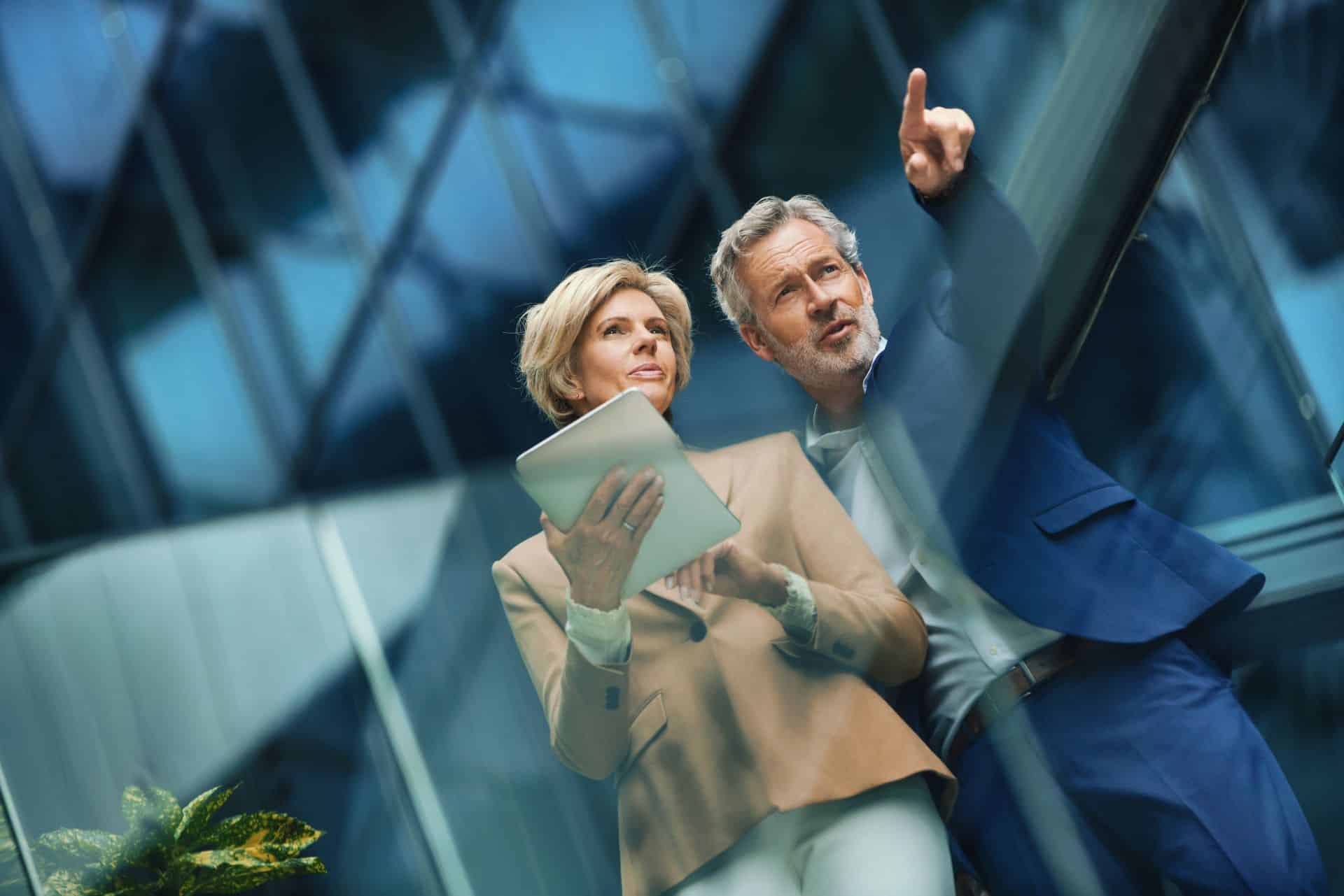 Zbliżenie, widok z dołu, rozmowa przed budynkiem biurowym. Patrzą na tablet cyfrowy, a mężczyzna wskazuje w dal.