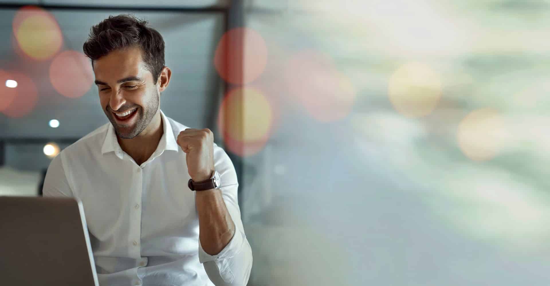 Meżczyzna w białej koszuli przed laptopem cieszy się z dobrej decyzji