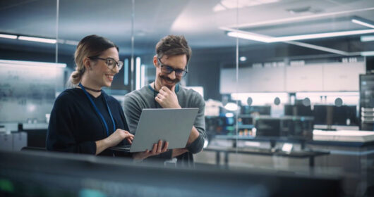 Dwójka współpracowników analizuje dane na laptopie w nowoczesnym biurze, symbolizując współpracę finansów z biznesem jako partnerów wspierających decyzje.