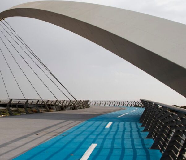 Nowoczesny most łukowy z wydzieloną niebieską ścieżką rowerową w przestrzeni miejskiej