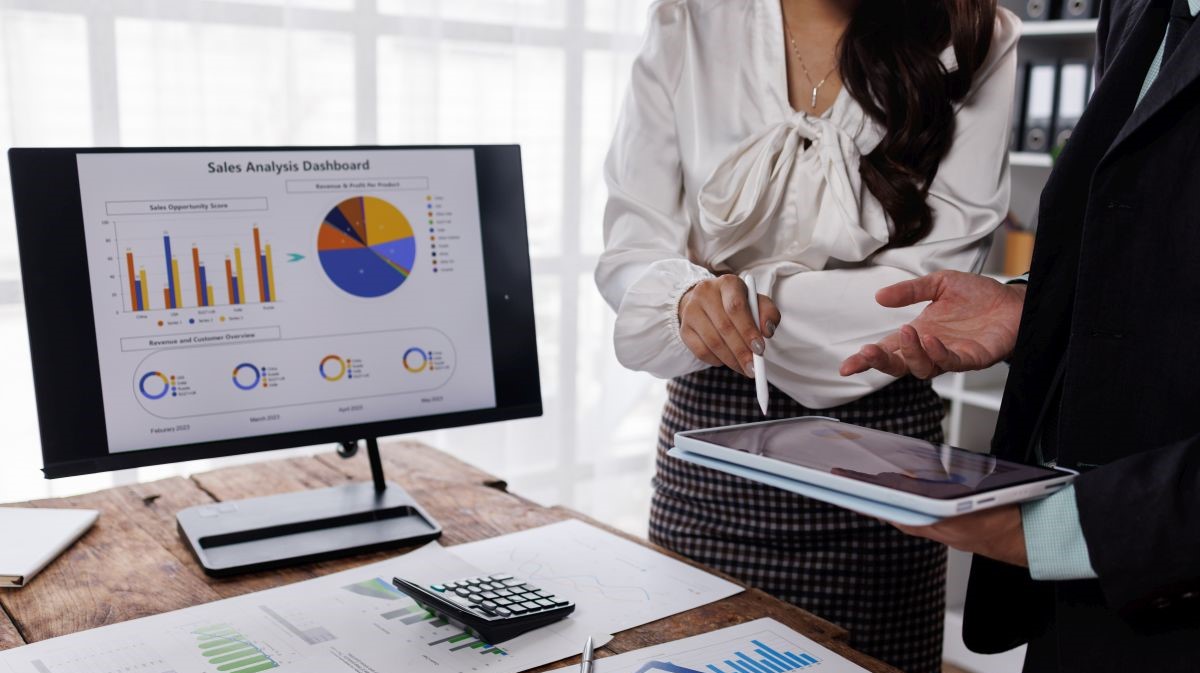 Business team analysing sales dashboard, financial charts, calculator, and tablet during a discussion about company performance, EBITDA, profit, margin, and cash flow.